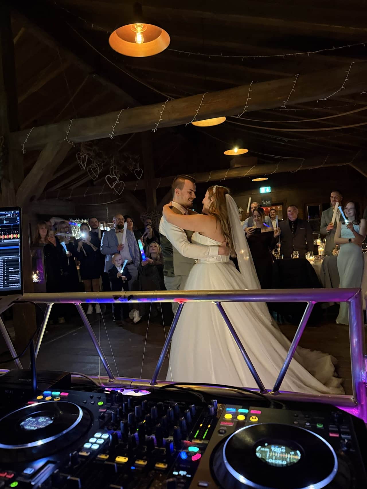 Blick vom DJ-Pult über den Controller auf das Brautpaar beim Tanz, dahinter Gäste mit Leuchtstäben