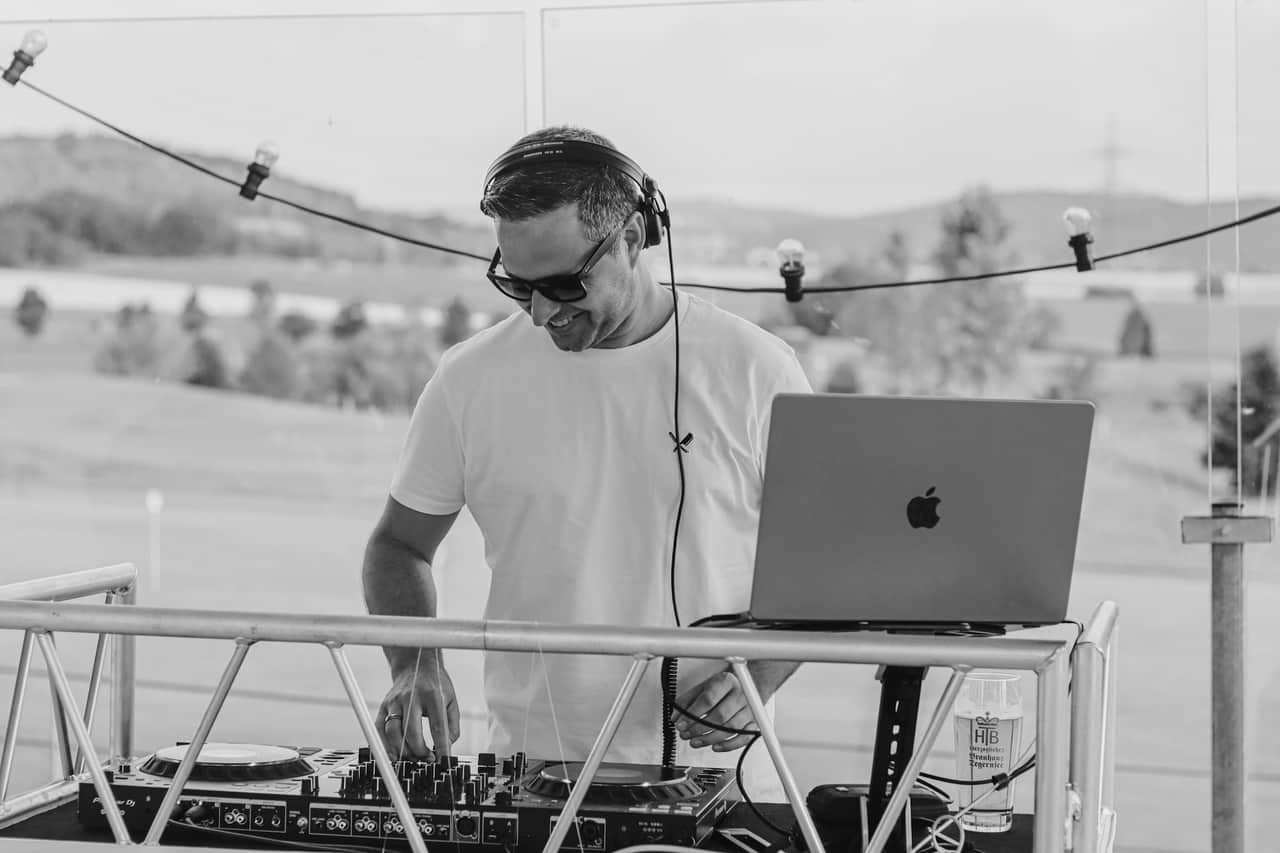 Alex am DJ-Pult mit Kopfhörern, die Hände am Controller, daneben der Laptop
