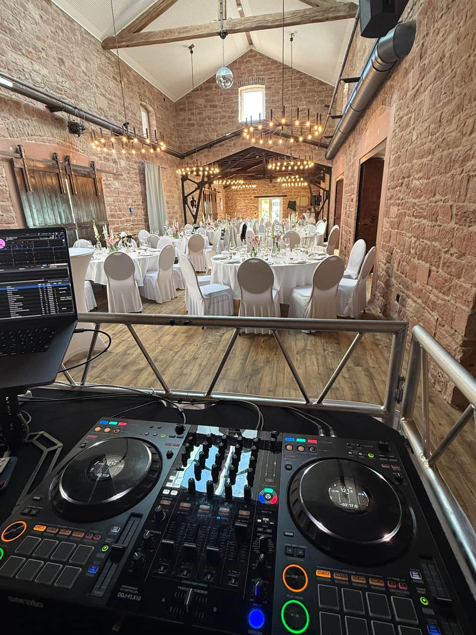 DJ-Pult mit Blick in einen festlich gedeckten Saal